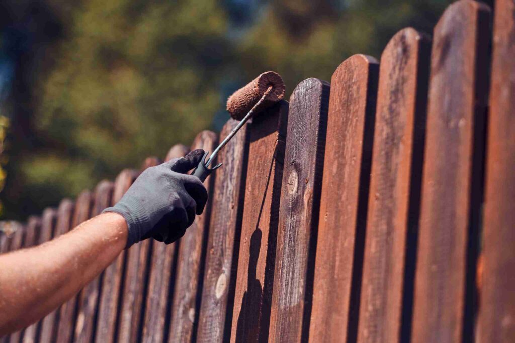 man protective gloves is painting wooden fence bright summer day scaled